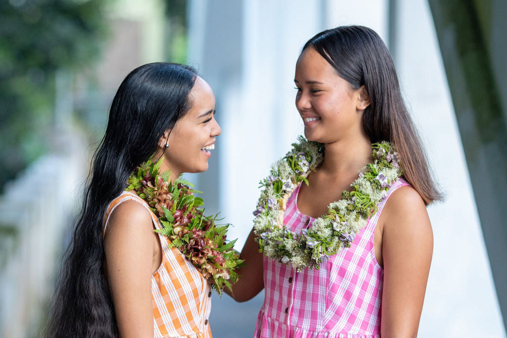 Two models in KAHUI Palaka looking at each other. One is wearing pink and the other orange.