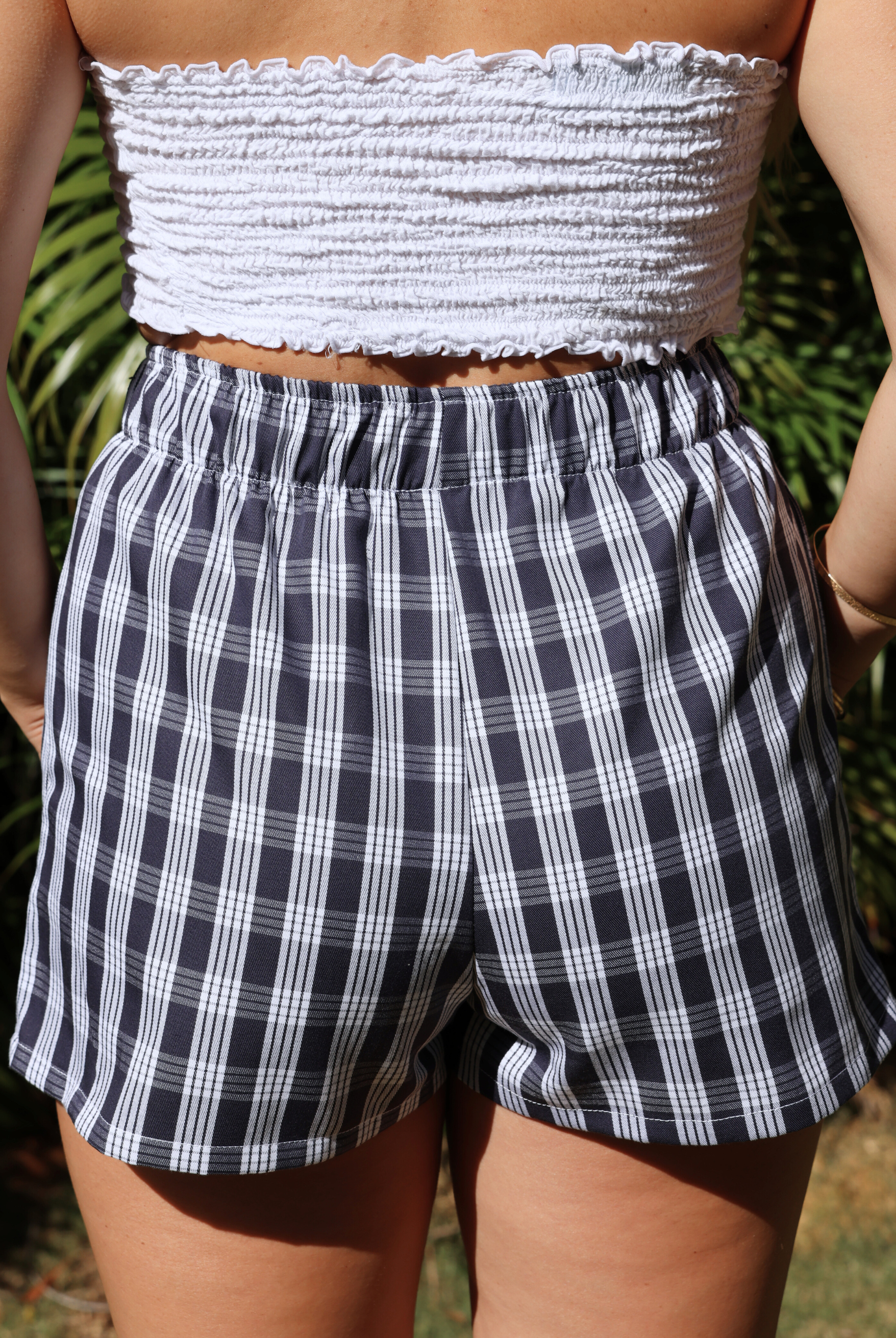 Wahine Holoholo Shorts 2.0 featuring a Palaka print, elastic waistband. Back view in bright outdoor lighting. Worn with a white bandeau.