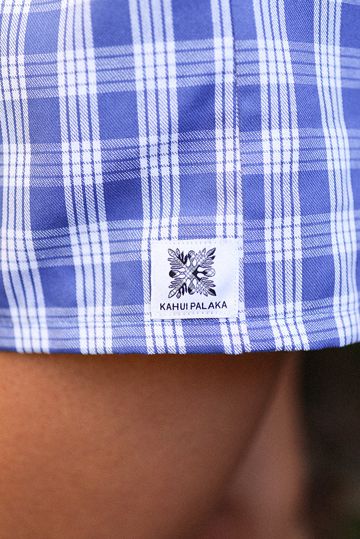 Wahine Holoholo Shorts 2.0 in Imua Blue with Palaka print, close-up of the bottom hem showcasing a logo patch.
