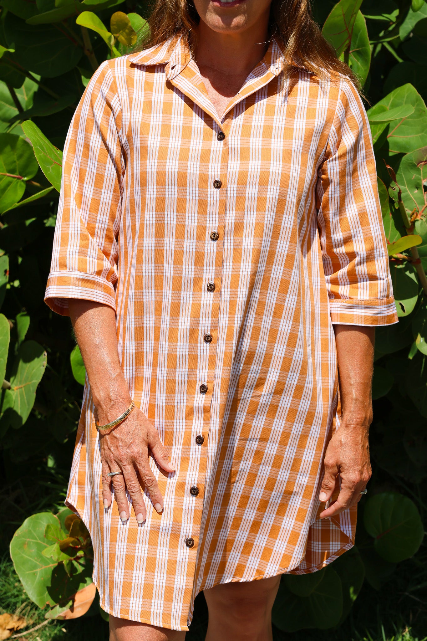 Kaunaʻoa Rust dress in Palaka pattern, button-down style with three-quarter sleeves. Outdoor setting with bright sunlight.