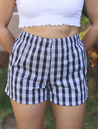Wahine Holoholo Shorts 2.0 feature a Palaka print, elastic waistband. Paired with a white cropped top, hands behind back.