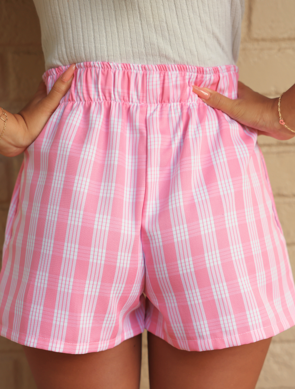 Wahine Holoholo Shorts 2.0 in Lokelani Light, featuring a pink Palaka pattern. Model poses with hands in pockets, showcasing the elastic waistband against a neutral background.