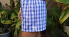 Wahine Holoholo Shorts feature an Imua Blue Palaka print. Side profile with garden plants in the blurred background.