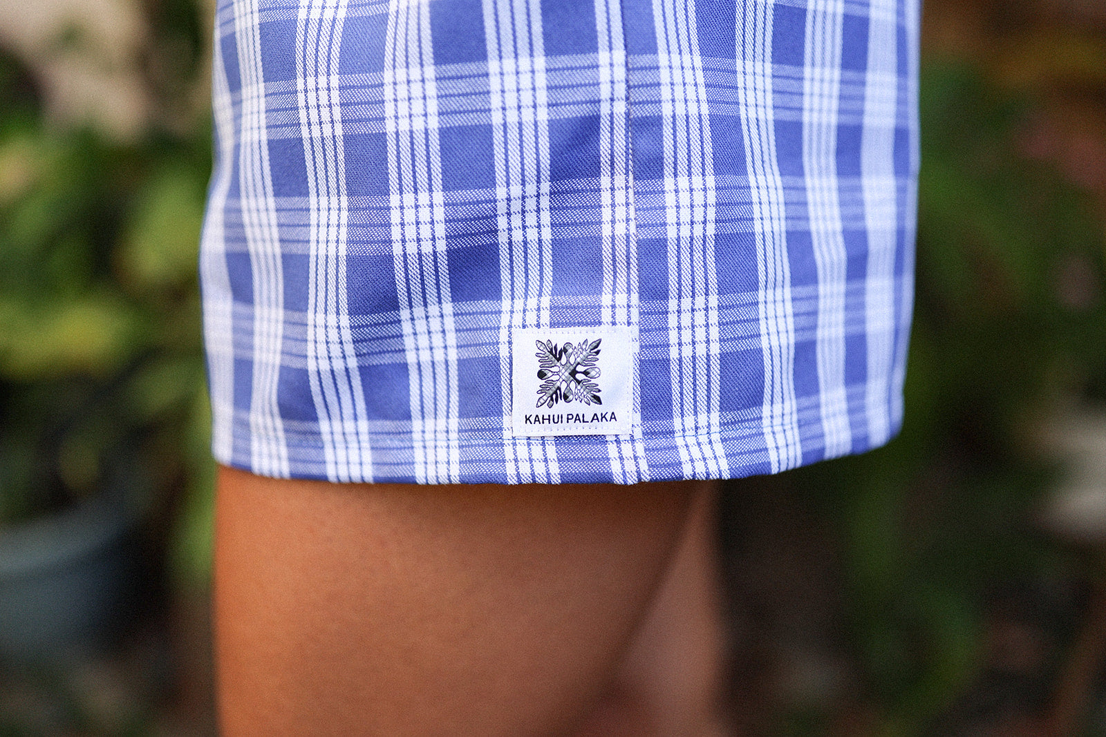 Wahine Holoholo Shorts 2.0 in Imua Blue with Palaka print, close-up of the bottom hem showcasing a logo patch.